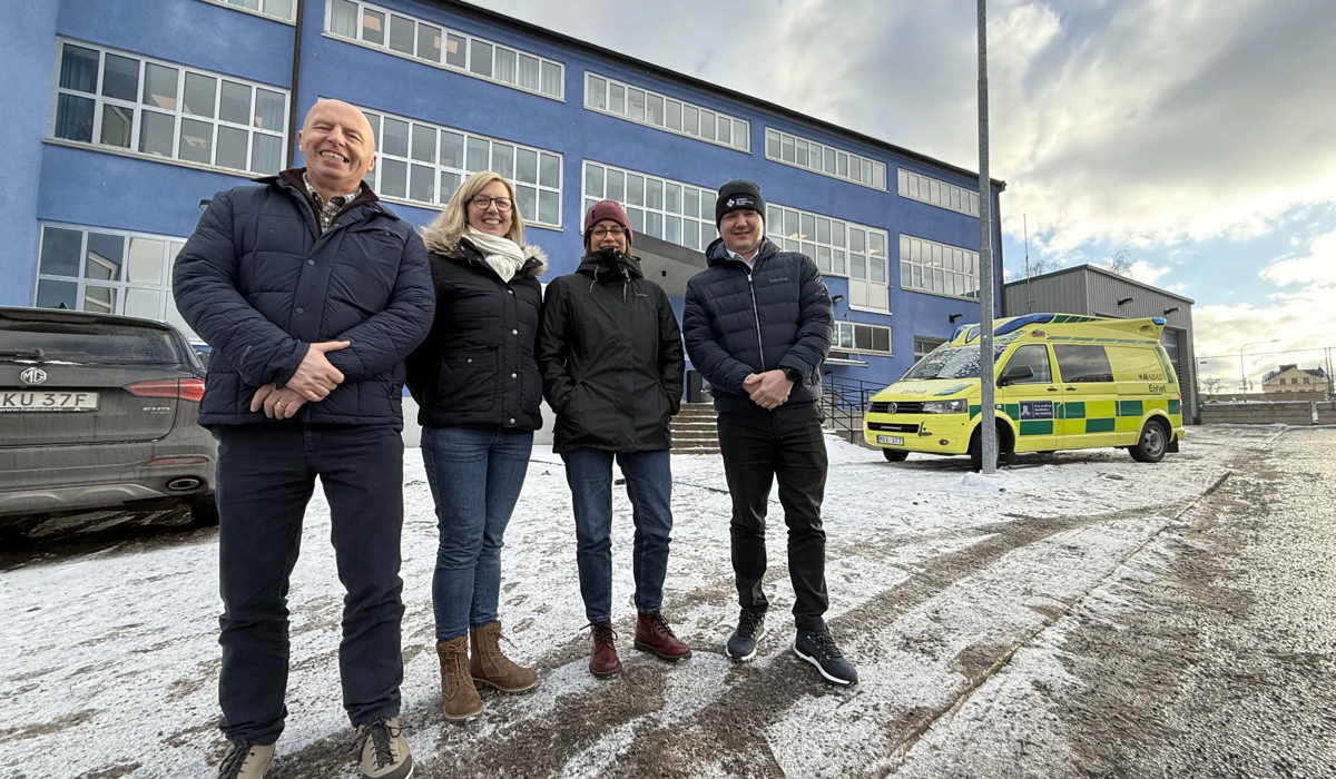 Fyra personer framf&ouml;r byggnad och ambulans