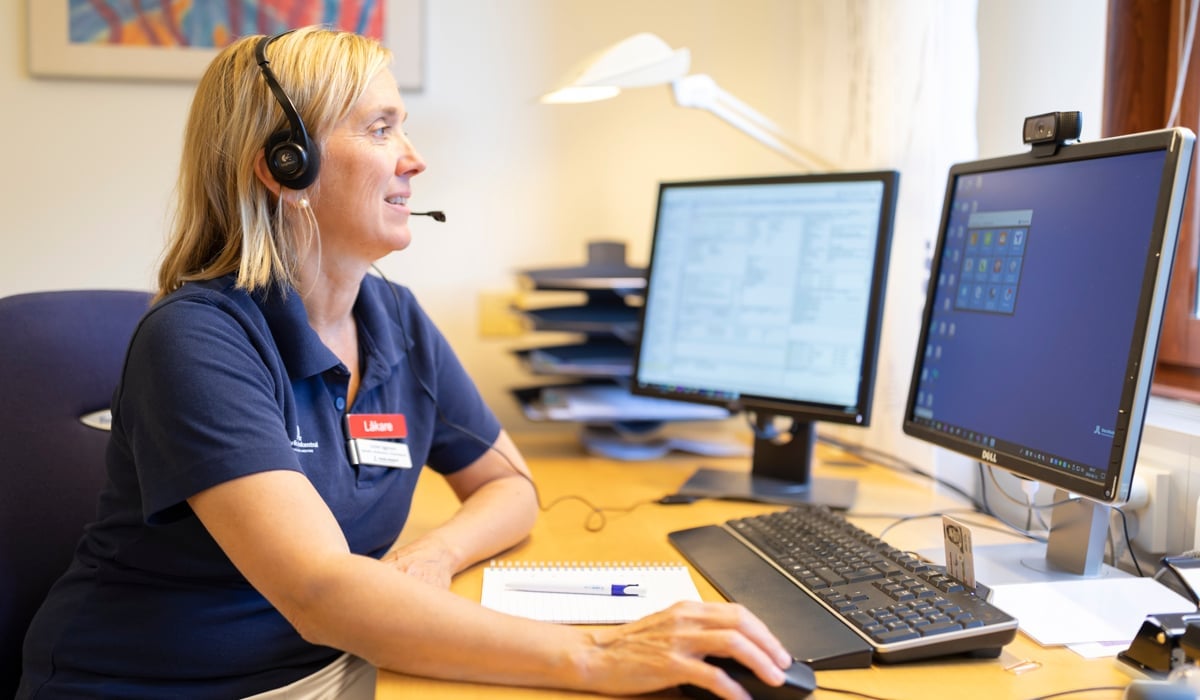 En kvinna sitter vid ett skrivbord med en bärbar dator och en datorskärm.