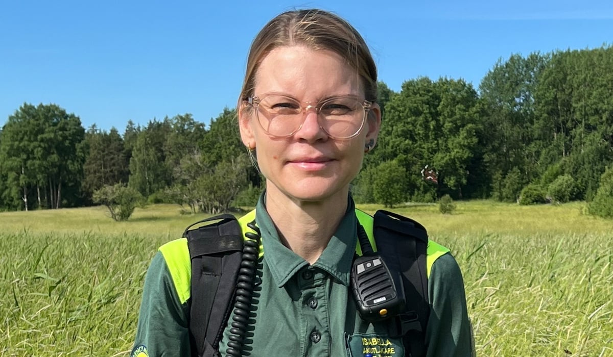 En kvinna i ambulanskläder står i gräset på en äng