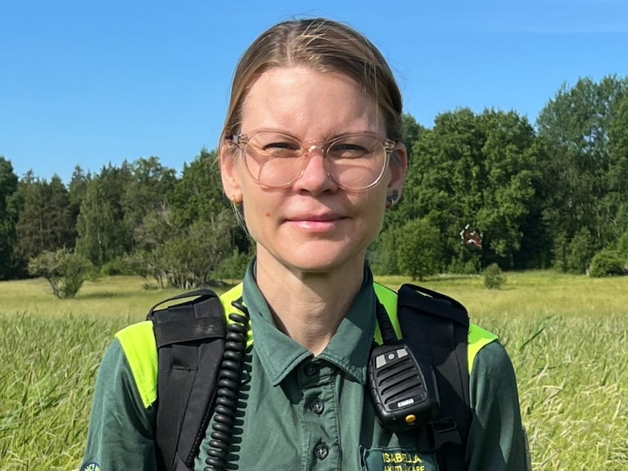 En kvinna i ambulanskläder står i gräset på en äng