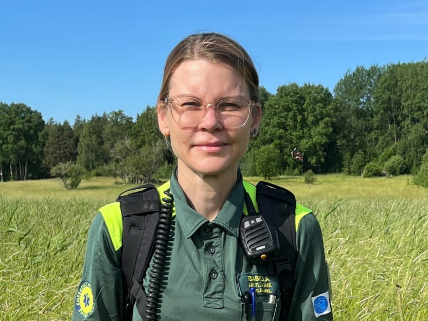 En kvinna i ambulanskläder står i gräset på en äng
