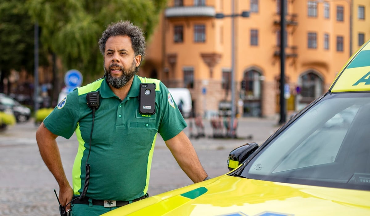 Ambulansmedarbetare står utomhus i stadsmiljö vid ambulans