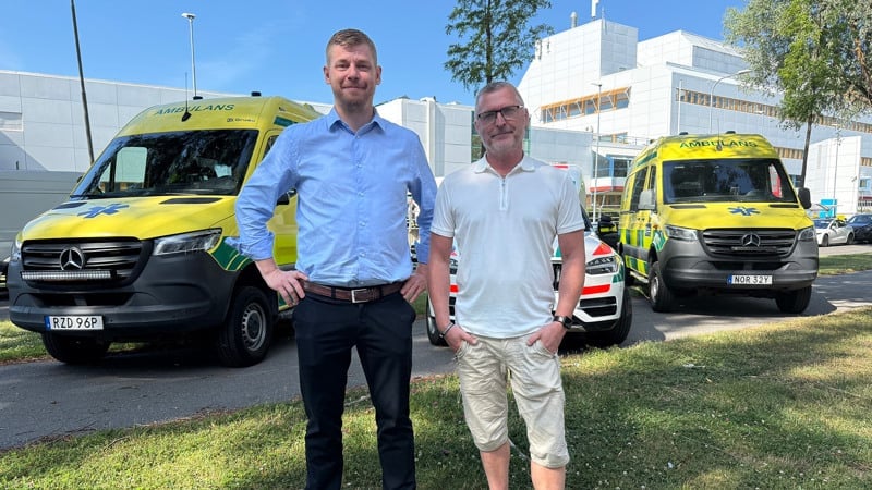 Två personer står utomhus framför tre ambulanser.
