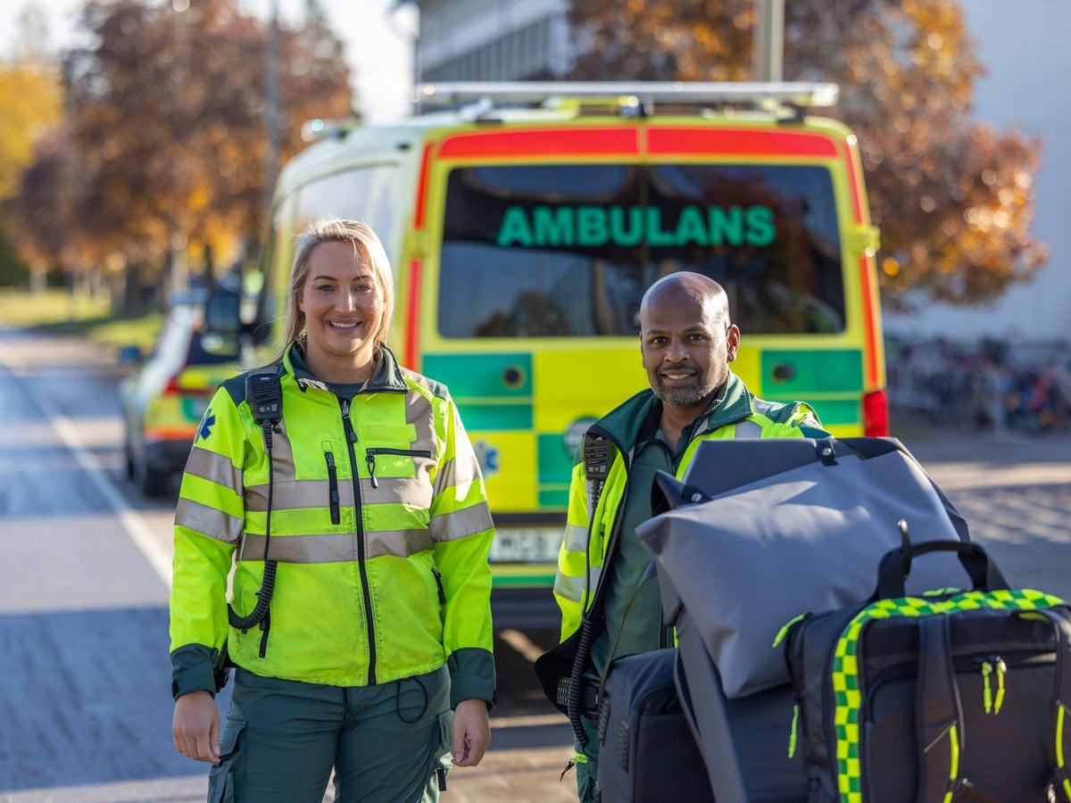 Två glada medarbetare med en bår som står framför en ambulans.